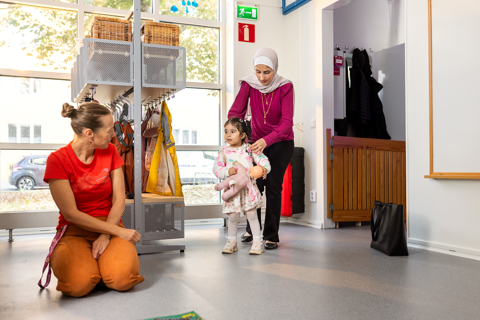 Vuxen hjälper litet barn som håller i en docka i en förskolemiljö
